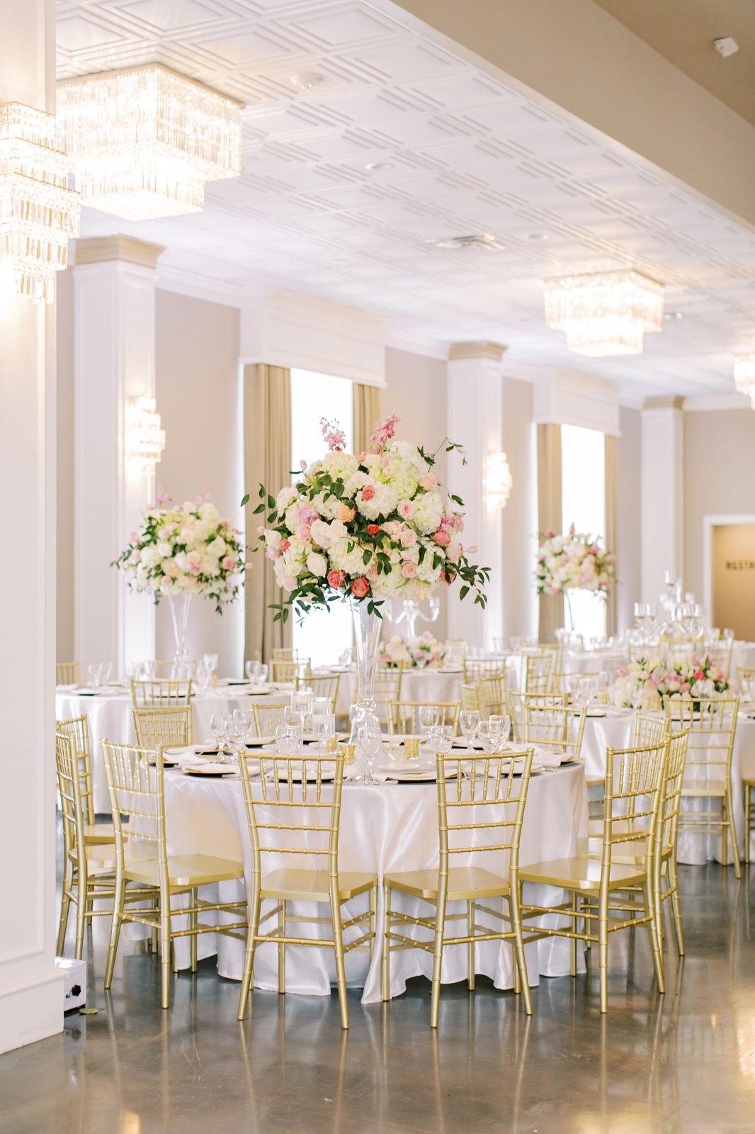 Grand reception ballroom set with floral centerpieces, gold chiavari chairs, and chandeliers