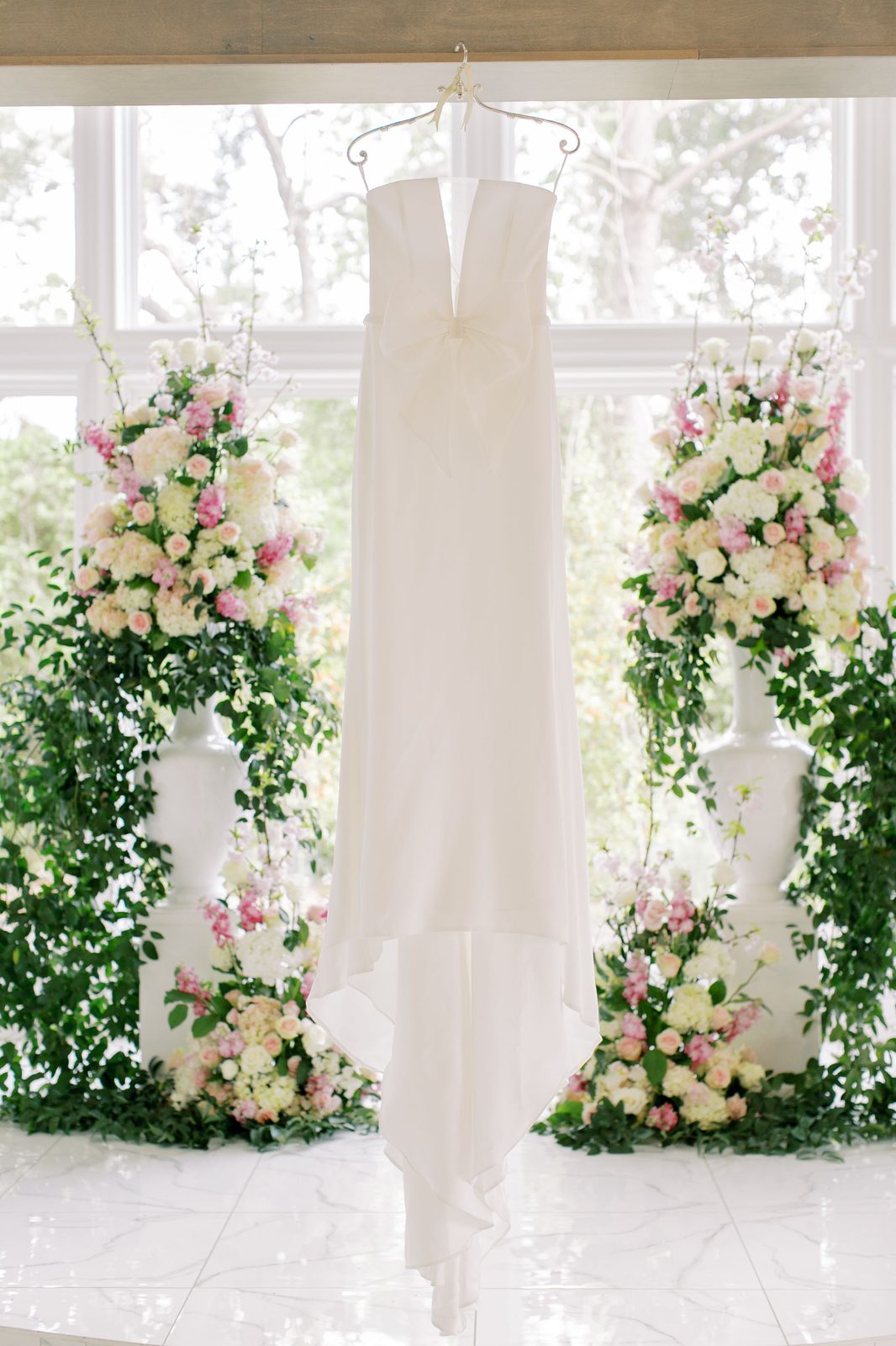 Wedding dress hanging in front of a pink and white floral arrangement