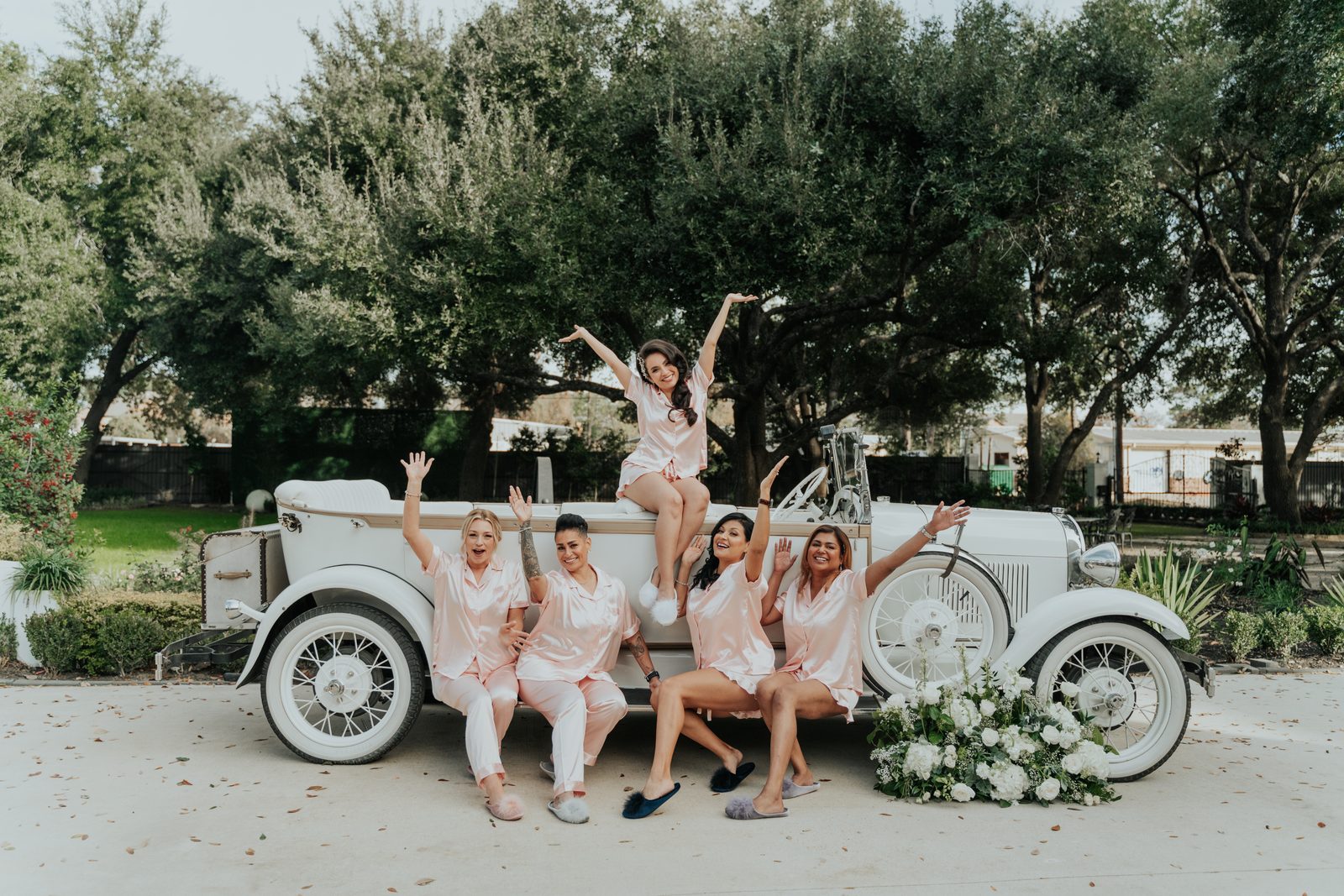 Bridesmaids in pink pajamas on a vintage car, getting ready