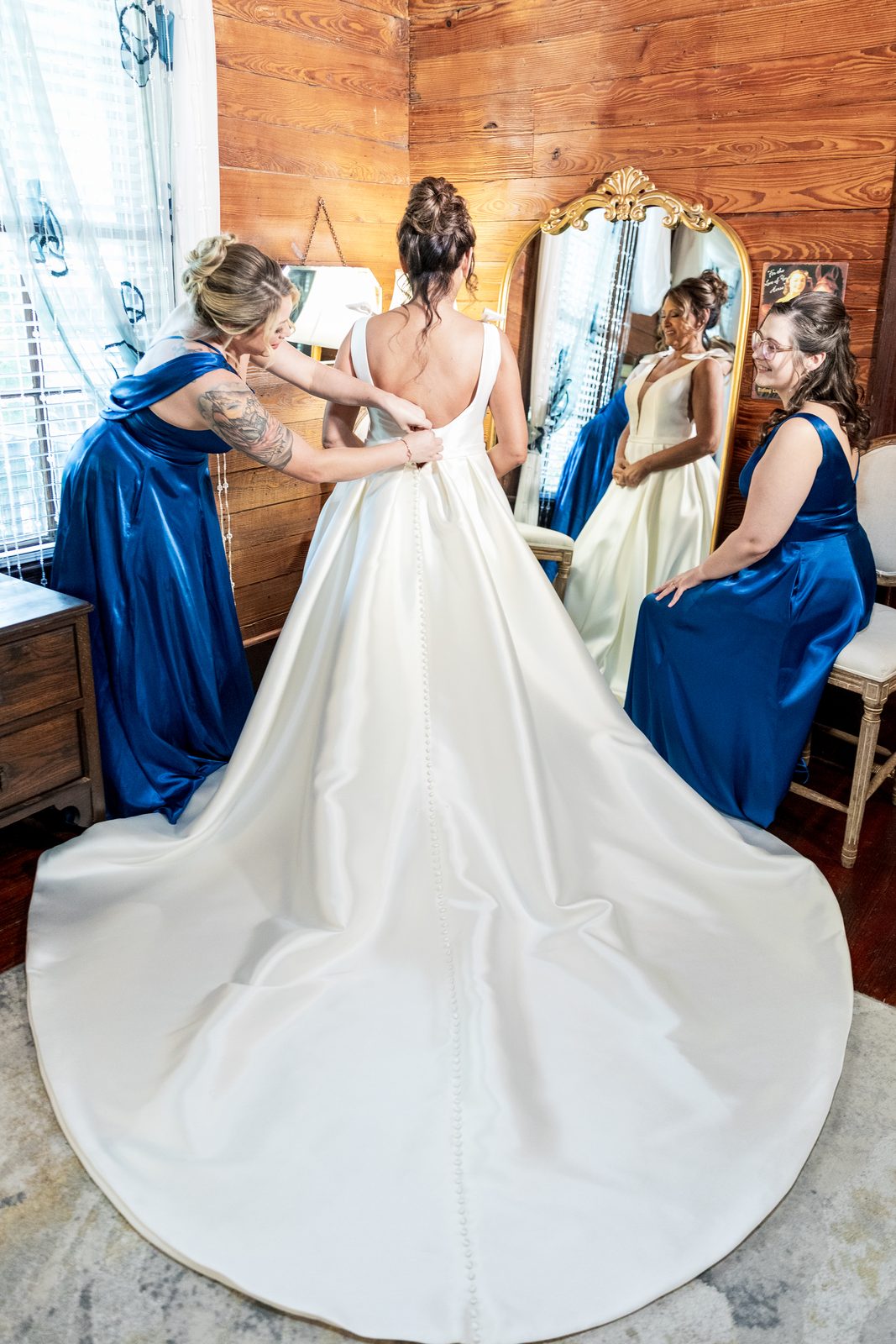 Bridesmaid buttoning the back of De's wedding gown
